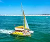 A colorful catamaran with passengers sails across blue waters near a coastline with some buildings in the distance