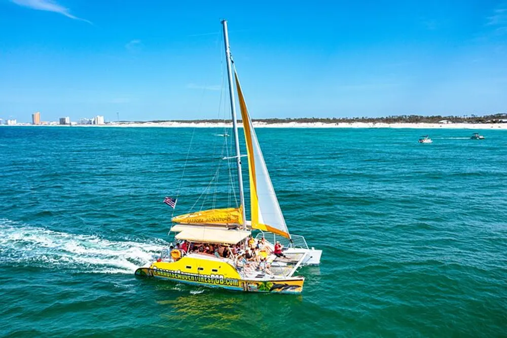A colorful catamaran with passengers sails across blue waters near a coastline with some buildings in the distance