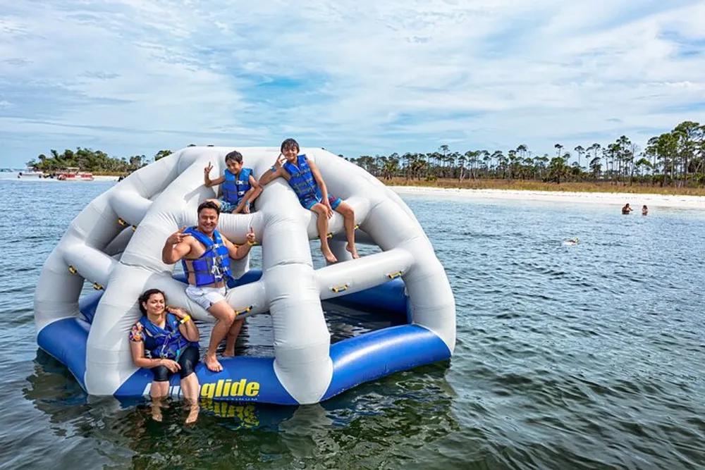 A group of people wearing life jackets are enjoying themselves on a large inflatable water trampoline by the beach