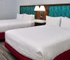 This image shows a modern hotel room with two neatly-made beds a shared headboard with built-in nightstands and a patterned aqua-blue backdrop