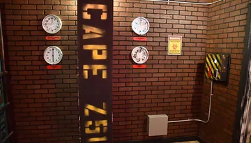 The image displays an industrial-themed room with brick walls, featuring a variety of analog gauges, a quarantine warning sign, and a pillar with text cutouts that cast shadows on the wall.