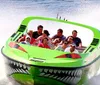 A group of people are experiencing a high-speed thrill ride on a boat designed to look like a menacing green creature with sharp teeth spraying water behind as it races forward