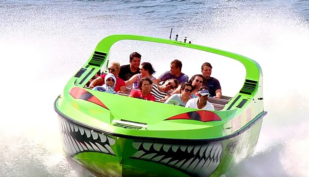 A group of people are experiencing a high-speed thrill ride on a boat designed to look like a menacing green creature with sharp teeth spraying water behind as it races forward