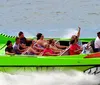 A group of people are experiencing a high-speed thrill ride on a boat designed to look like a menacing green creature with sharp teeth spraying water behind as it races forward