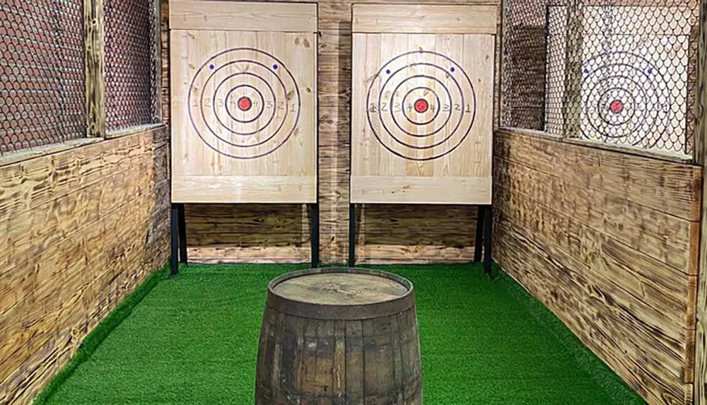 This image shows a setup of three axe-throwing targets in a rustic-themed area with artificial grass flooring and protective mesh on the sides