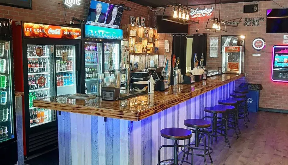 This image features the interior of a well-lit empty bar with stools a wooden counter multiple beer taps a television broadcasting news and refrigerated beverage display cases