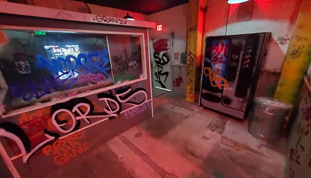 The photo shows a gritty urban scene with a vending machine and window covered in graffiti inside what appears to be a dimly lit alleyway or passageway with brick walls