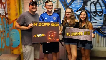 Four people are happily posing with signs indicating that they successfully completed an escape room challenge.