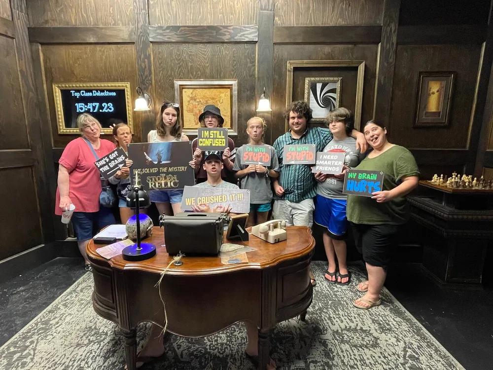 A group of people poses with humorous signs celebrating their completion of an escape room challenge with a detective theme
