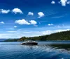 A motorboat cruises on a clear blue lake against a backdrop of forested hills and a sky dotted with fluffy clouds