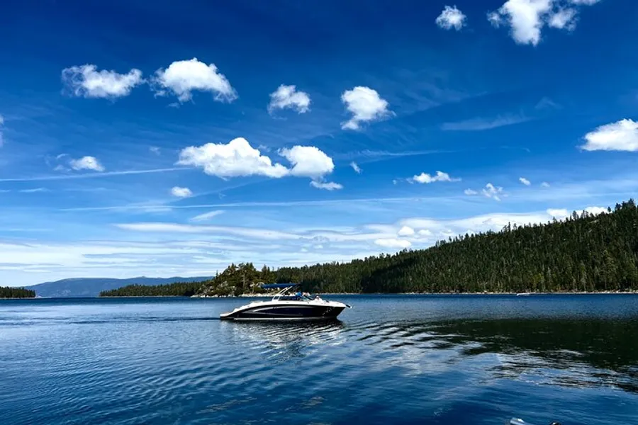 A motorboat cruises on a clear blue lake against a backdrop of forested hills and a sky dotted with fluffy clouds.