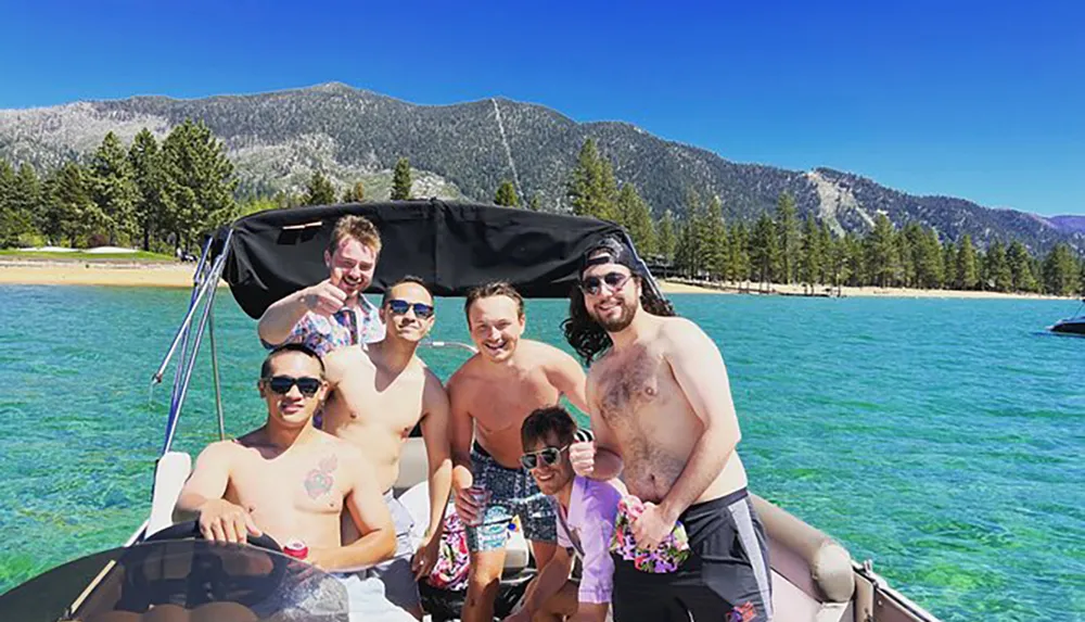 A group of friends is enjoying time together on a boat with clear blue waters and a mountainous backdrop on a sunny day