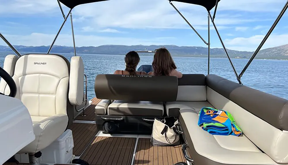 Two people are sitting and enjoying the view of a lake from the back of a boat