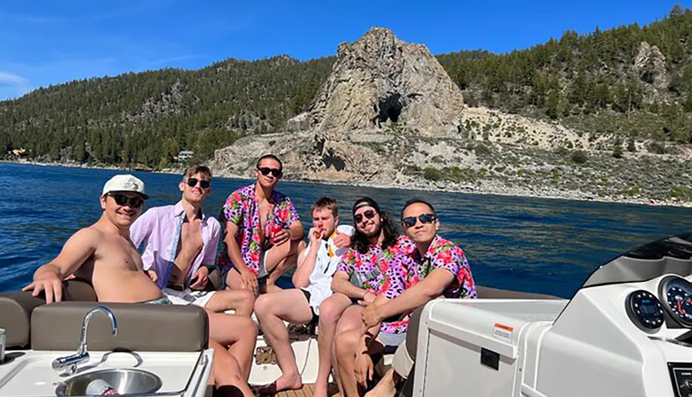 A group of friends wearing vibrant shirts is enjoying their time on a boat with a scenic rocky coastline in the background