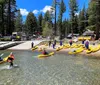 A group of people wearing life vests are smiling and paddling in tandem yellow kayaks on a lake with a backdrop of forested hills and clouds