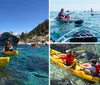 A group of people wearing life vests are smiling and paddling in tandem yellow kayaks on a lake with a backdrop of forested hills and clouds