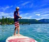 Three people in wetsuits are striking triumphant poses while standing on paddleboards in a clear blue lake with a scenic mountainous backdrop