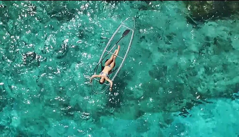 A person is lying on a clear transparent paddleboard over a turquoise sea