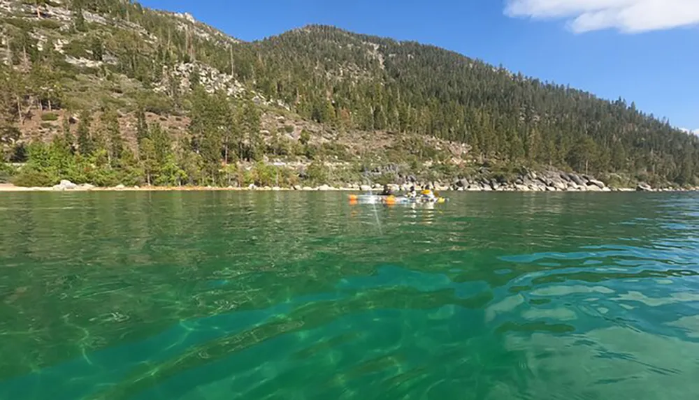 A group of people is kayaking over the clear turquoise waters of a lake near a forested mountainous area