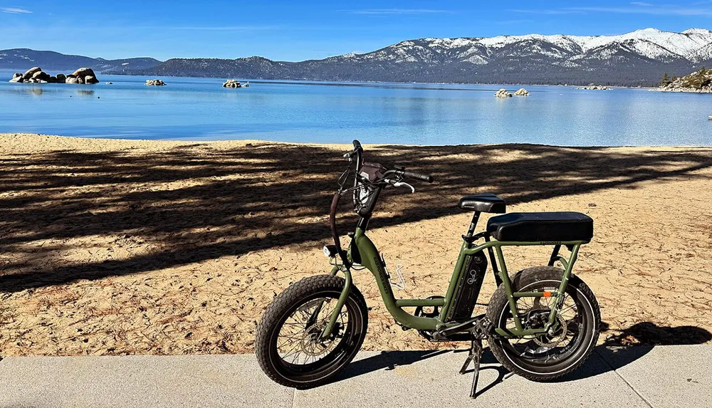 An electric bike is parked on a sunny lakeside with a view of mountains in the background