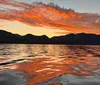 A fiery sunset paints the sky and reflects on the rippled surface of a lake against a backdrop of dark mountains