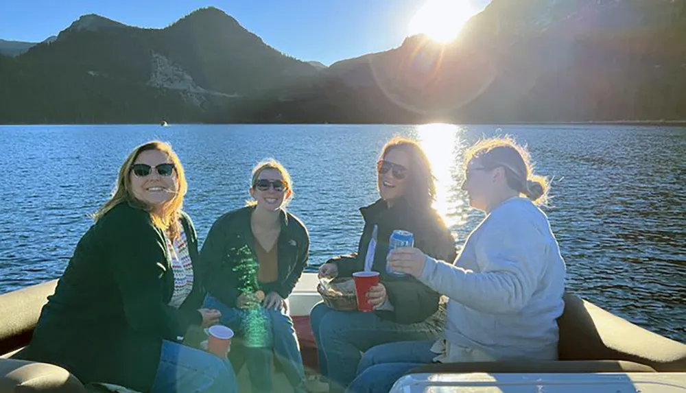 Four people are enjoying a sunny day on a boat with a scenic mountainous backdrop creating a casual and joyful atmosphere