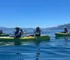 Four individuals are enjoying kayaking on a calm lake with a picturesque mountainous backdrop
