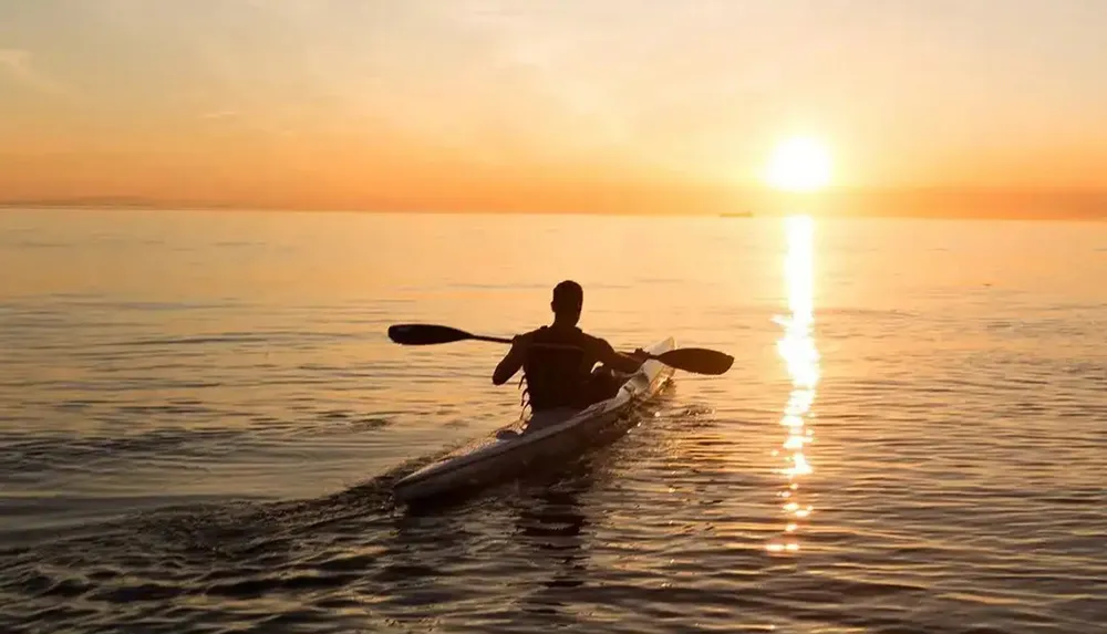 A person is kayaking on a calm body of water during a beautiful sunset