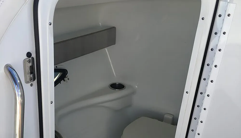 The image shows a compact simple marine or RV toilet compartment with minimal fixtures and a small entry door