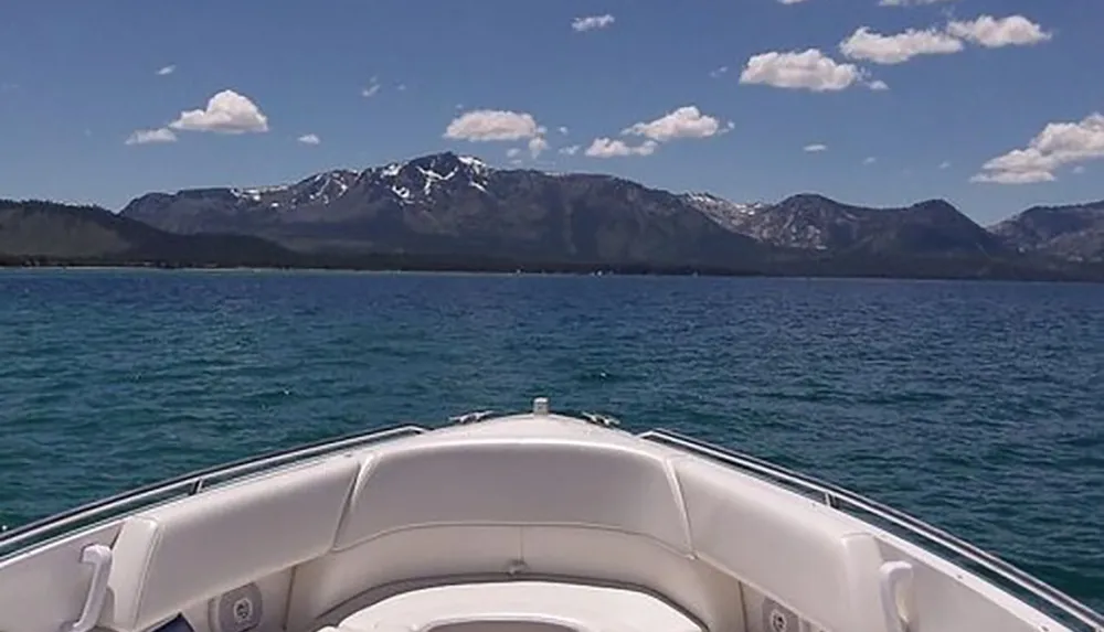 A boat is cruising on a clear blue lake with a backdrop of rugged snow-capped mountains under a partly cloudy sky
