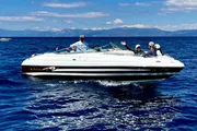 A group of people are enjoying a sunny day on a white speedboat on a calm blue sea.