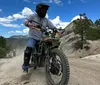 A dirt bike rider in full gear takes to a dusty trail amidst a wooded area under a clear blue sky