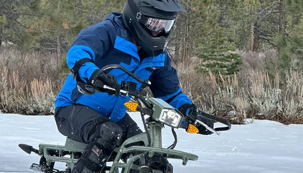 A person in a blue jacket and helmet is riding a motorcycle across a snowy terrain