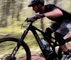 Two mountain bikers are navigating a rocky trail amidst trees under a clear blue sky