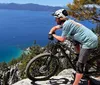 Two mountain bikers are navigating a rocky trail amidst trees under a clear blue sky