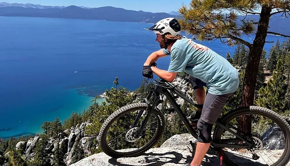 A person is mountain biking on rocky terrain overlooking a beautiful blue lake
