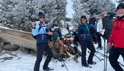 A group of happy hikers is posing with their cards in a snowy forest setting.