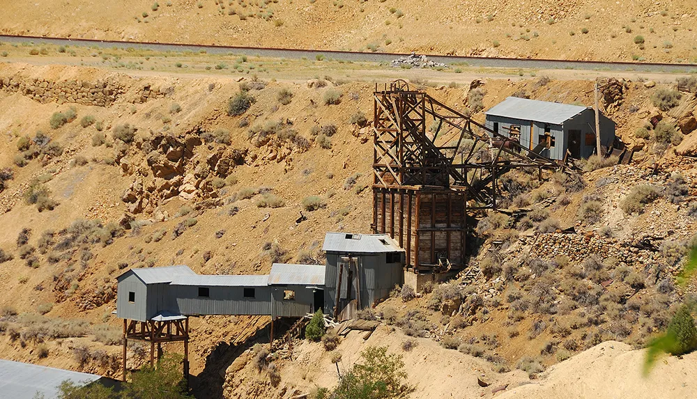 The image shows an abandoned mining structure with wooden buildings and rusted supports set against a dry hilly landscape
