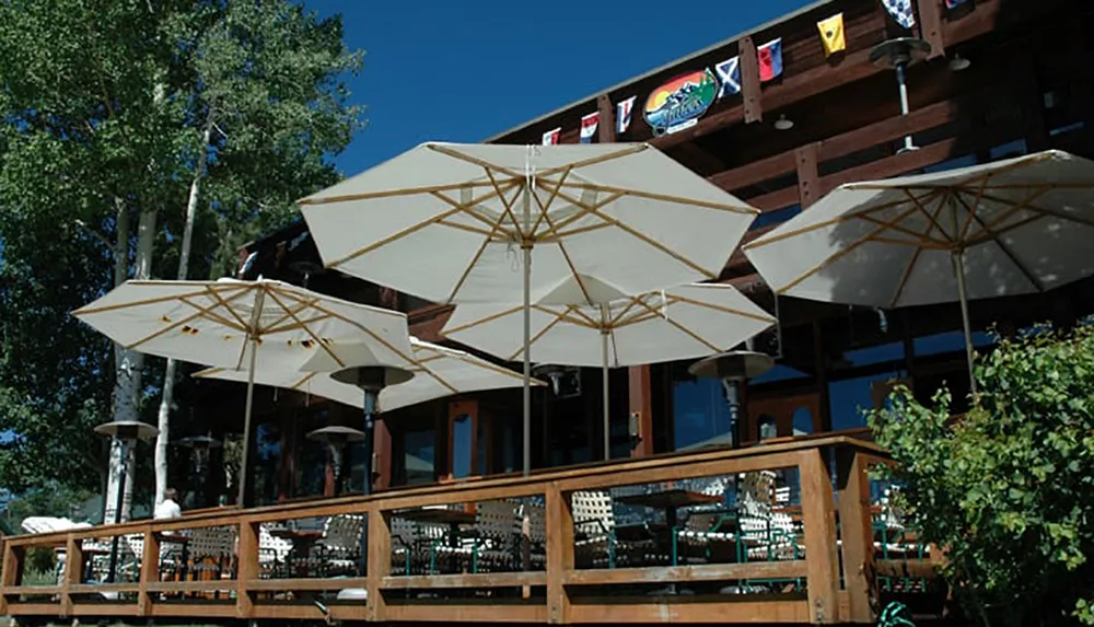 The image shows a sunny outdoor seating area of a restaurant with open umbrellas and flags from various countries displayed on the upper deck