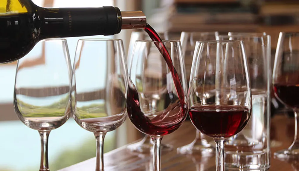 Red wine is being poured into a row of glasses against a blurred background