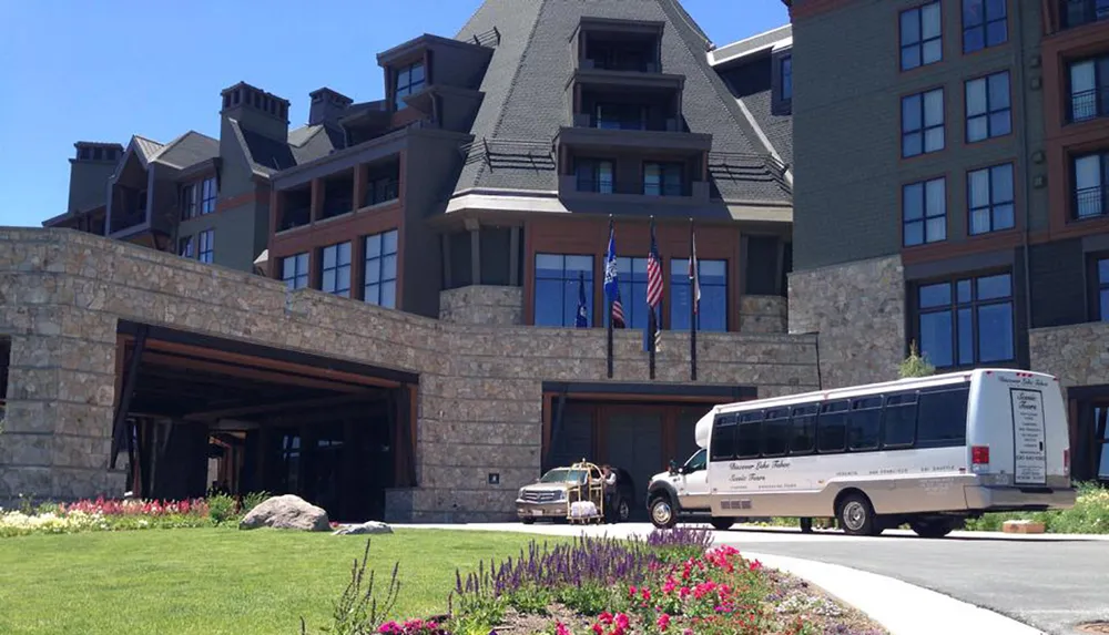 The image shows a large multi-story building with a stone facade and a steeple-like roof flanked by the United States flag and other flags with a shuttle bus parked in front