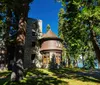 This is a photo of a stately historic house with stone foundations and a round turret surrounded by mature trees under a clear blue sky