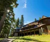 This is a photo of a stately historic house with stone foundations and a round turret surrounded by mature trees under a clear blue sky