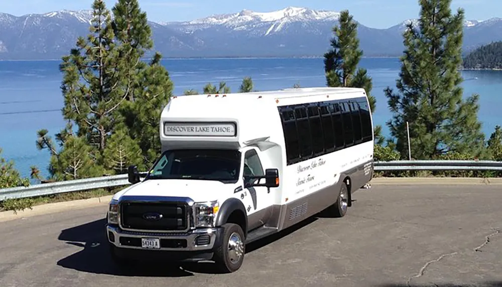 A tour bus with the label Discover Lake Tahoe is parked overlooking the picturesque blue waters of Lake Tahoe with snow-capped mountains in the distance