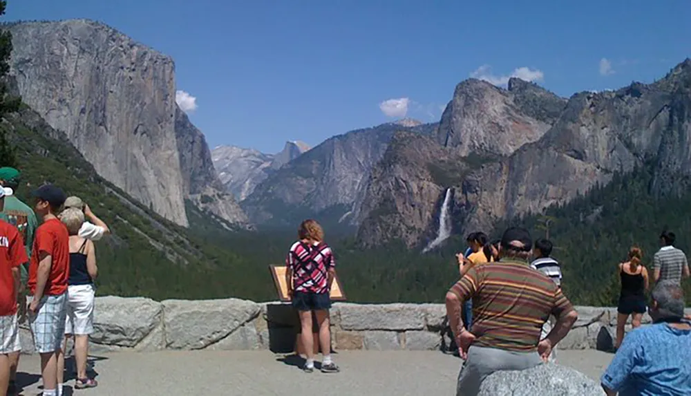 Tourists are enjoying the scenic view of a waterfall and granite cliffs at Yosemite National Park