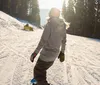 A snowboarder in colorful winter gear is performing a trick on a sunny mountain slope with clear blue skies in the background