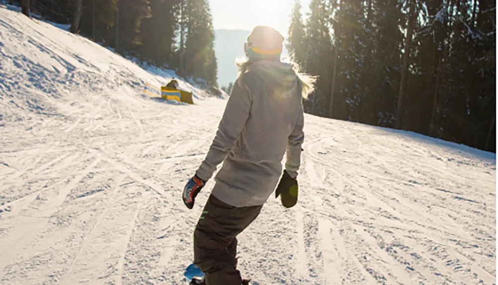 A person is walking uphill on a snowy slope likely at a ski resort amid a winter landscape bathed in sunlight