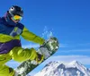 A snowboarder in colorful winter gear is performing a trick on a sunny mountain slope with clear blue skies in the background