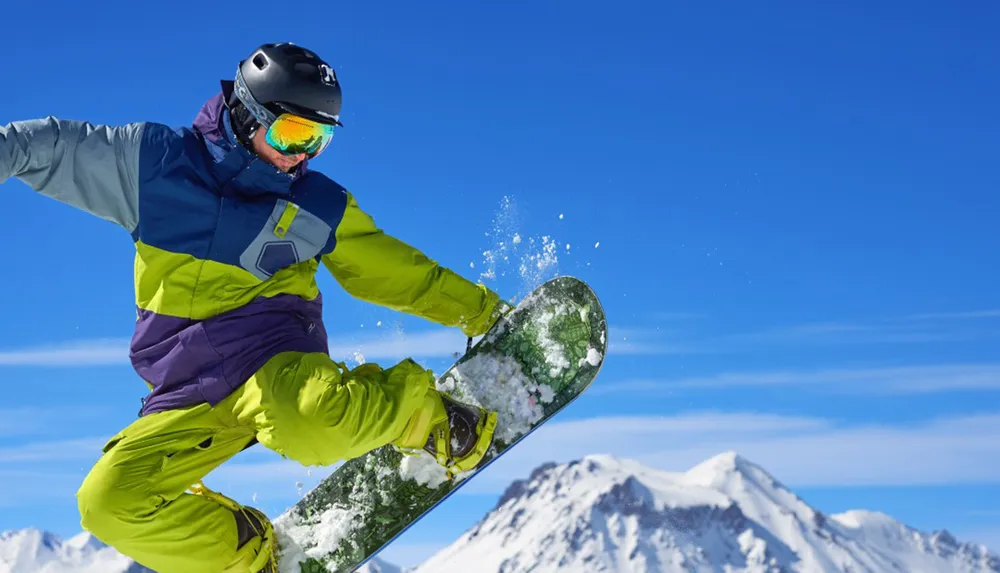 A snowboarder in colorful winter gear is performing a trick on a sunny mountain slope with clear blue skies in the background