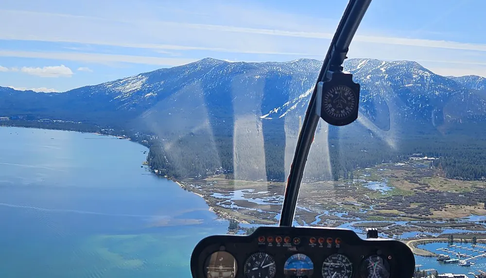The image shows a picturesque view from the cockpit of a helicopter overlooking a coastal landscape with mountains trees and water